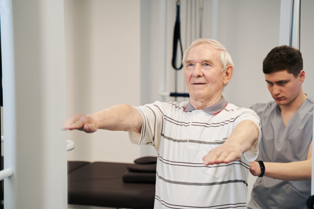 Elderly man engaging in physical therapy exercises with a therapist, assessing mobility and physical abilities in a clinical setting.
